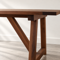 Close-up of solid walnut wooden table with a breadboard end and angled trestle-style legs.