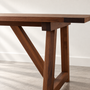 Close-up of solid walnut wooden table with a breadboard end and angled trestle-style legs.