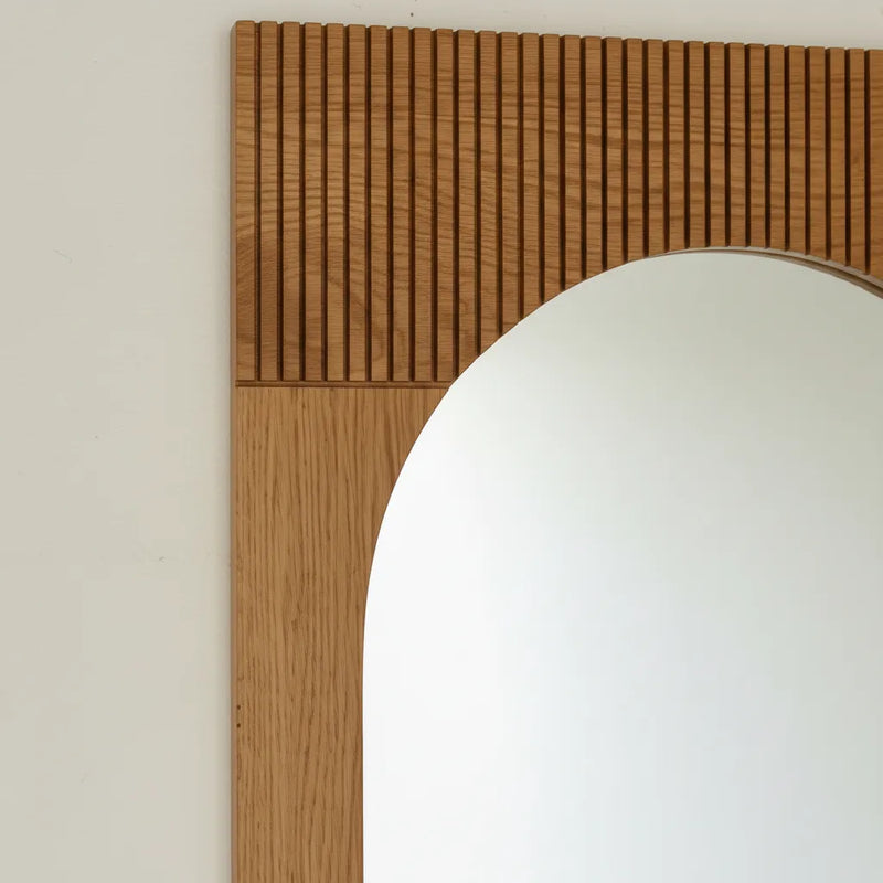 A close-up of a Bixby wooden wall mirror frame with a fluted top section and a smooth lower section.