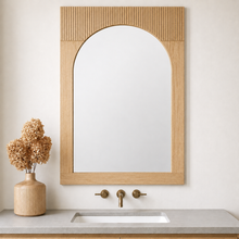 Bixby solid wood arched rectangular wall mirror with a light natural wood frame and vertical fluting at the top mounted above a bathroom vanity.