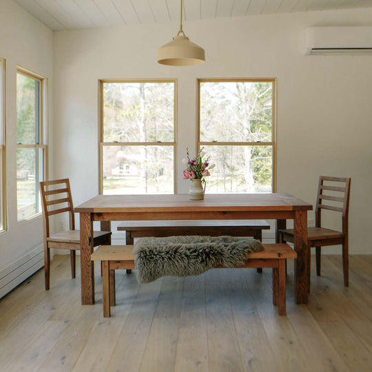 Dining room with wooden table and chairs, large windows, and a rug on light wood flooring.