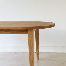 Close-up of white oak wood dining table showing the rounded top edge and tapered legs.