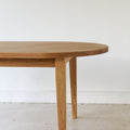 Close-up of white oak wood dining table showing the rounded top edge and tapered legs.