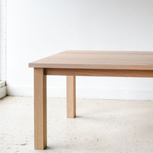 A light natural oak dining table with a rectangular top and four sturdy block legs, Parsons style design.