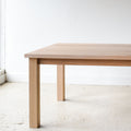 A light natural oak dining table with a rectangular top and four sturdy block legs, Parsons style design.