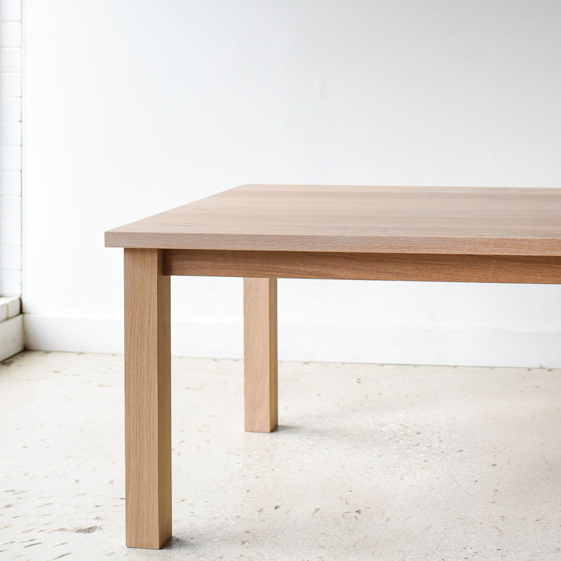 A light natural oak dining table with a rectangular top and four sturdy block legs, Parsons style design.