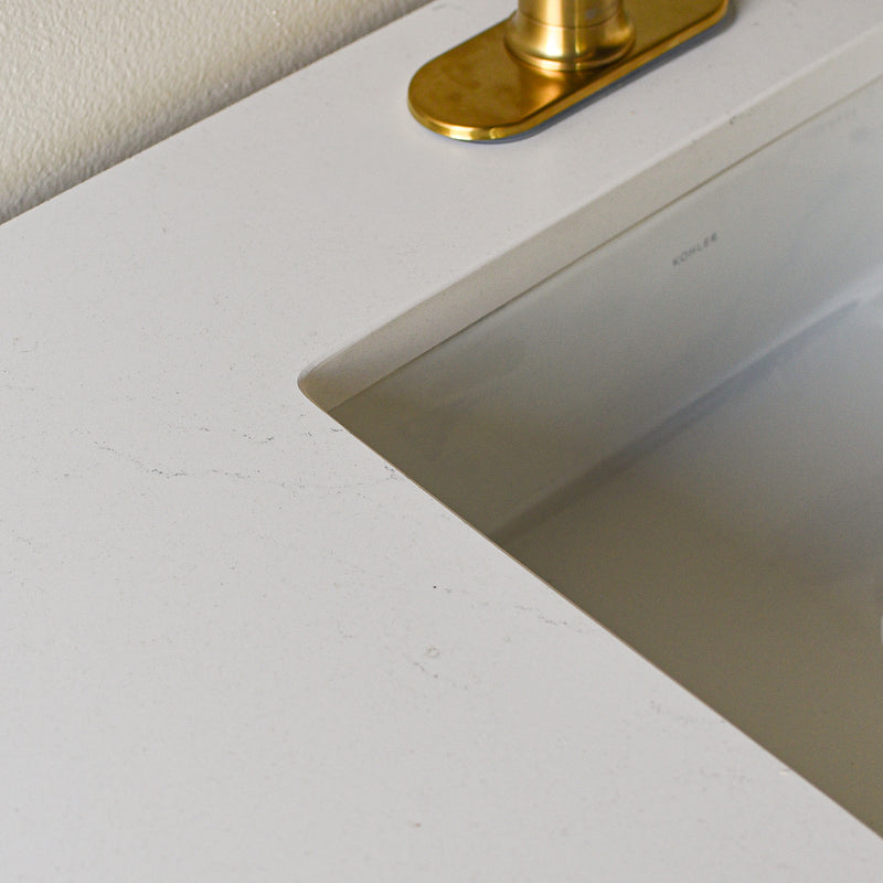 A close-up of soft white quartz countertop with subtle veining with a rectangular sink.
